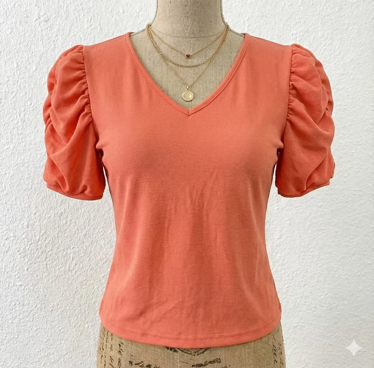 Blusa confeccionada en tela suave y ligera, color coral, con escote en V, manga corta abullonada y corte entallado, ideal para uso diario o casual.